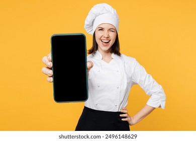 Young chef cook baker woman wears white shirt black apron uniform toque chefs hat hold use blank screen area mobile cell phone wink blink eye isolated on plain yellow background. Cooking food concept - Powered by Shutterstock