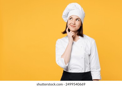 Young chef cook baker woman wear white shirt black apron uniform toque chefs hat put hand prop up on chin, lost in thought and conjectures isolated on plain yellow background studio. Cooking concept - Powered by Shutterstock