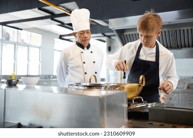 young chef cooking some food and senior chef beside him in the kitchen - Powered by Shutterstock