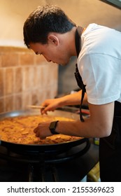 Young Chef Preparing Paella In A Large Frying Pan.