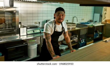 Young chef is smiling while standing on a large kitchen. Male cook is working in a large restaurant cuisine. Worker in an apron in the cook room