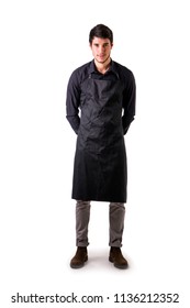 Young Chef Or Waiter Posing, Wearing Black Apron And Shirt Isolated On White Background