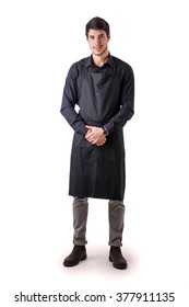 Young Chef Or Waiter Posing, Wearing Black Apron And Shirt Isolated On White Background