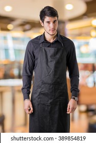 Young Chef Or Waiter Wearing Black Apron In Restaurant