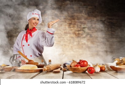 Young chef woman cooker ready for food preparation. Raw ingredients served on wooden table, blur brick wall on background