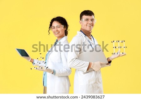 Young chemists with molecular models and tablet computer on yellow background