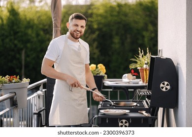 Young chief in apron preparing to cook steak on BBQ grill. Side view of man preparing food for video blog - Powered by Shutterstock