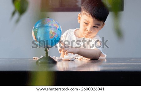 A young child boy is looking and pointing a planet earth model while sitting at outdoor. Kids discovering world Concept. 