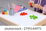A young child connects interlocking math cubes at a desk with pencils and notebooks.