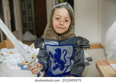 Young child dressed as a knight with toy sword, sitting on bed, imaginative play, wearing medieval costume, bedroom scene, childhood, creativity, playful, happy expression, knight armor - Powered by Shutterstock