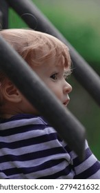 Young child exploring elevated play equipment at playground while observing surroundings highlighting curiosity, confidence and authentic outdoor family lifestyle