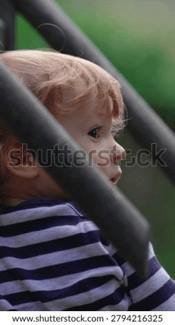 Young child exploring elevated play equipment at playground while observing surroundings highlighting curiosity, confidence and authentic outdoor family lifestyle