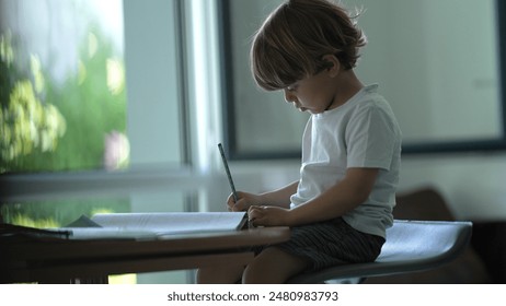 Young Child Focused on Writing, Sitting at a Desk in a Brightly Lit Room - Powered by Shutterstock