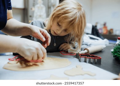 A young child focuses intently as an adult helps with holiday cookie baking. They surrounded by festive decorations and baking tools. Christmas craft - Powered by Shutterstock