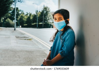 Young Child Girl Wearing Protective Face Mask Outdoors Sitting At Bus Stop Against Corona Virus