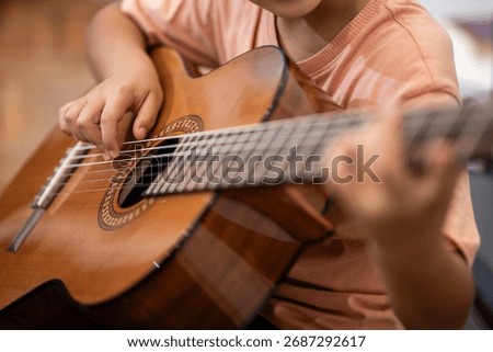 Young child hands picking strings on a wooden acoustic guitar, learning music, practicing a new hobby or training