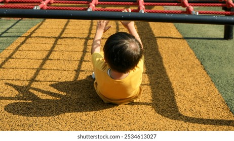 A young child hangs upside down on a red and black playground climbing frame. - Powered by Shutterstock