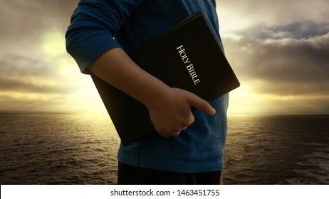 Young Child Holding Bible In Front Of The Sea