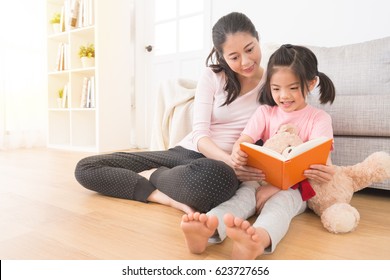 young child holding cute teddy bear with mother sitting on the wooden floor happy watch the family photo album together to browse the holiday memories enjoy leisure time with her mom.