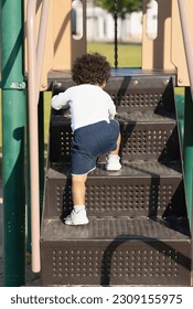 A young child is learning to climb up steps. Toddler is working on gross motor at the playground. Active Kid is outside stepping up on equipment too big for his small body. daycare, camp, school, fun