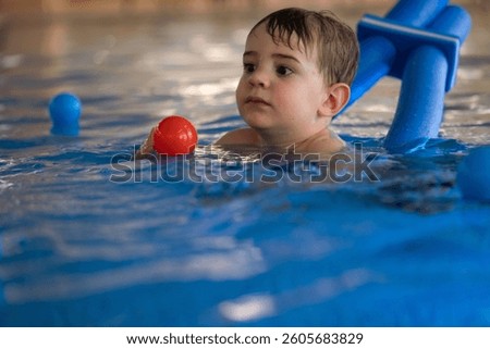 Young child learning to swim with floatation device, playing with ball, enjoying time in pool
