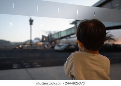 A young child is looking out a window at a busy airport. The sce