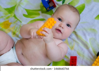 A young child is lying on the bed and playing with a plastic toy. The child holds a yellow detail of the designer. The child lies on white sheets with yellow and green spots. Toys lie around.  - Powered by Shutterstock