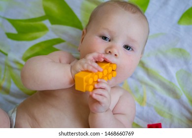 A young child is lying on the bed and playing with a plastic toy. The child holds a yellow detail of the designer. The child lies on white sheets with yellow and green spots. Toys lie around.  - Powered by Shutterstock