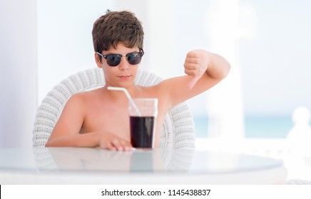 Young Child On Holidays Drinking Soda With Angry Face, Negative Sign Showing Dislike With Thumbs Down, Rejection Concept