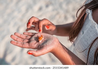 A young child playing with a hermit crab which she holds in the palm of her hand at the beach - Powered by Shutterstock