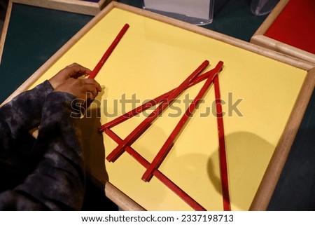A young child playing with red long sticks, enjoying their time creating imaginative structures