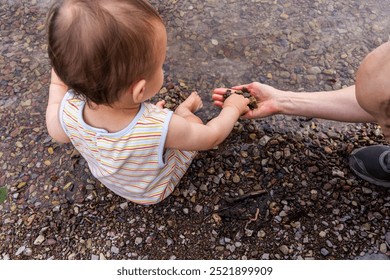 A young child sits at the lakeshore, exploring pebbles with a parent's guidance, capturing a moment of curiosity and connection in Waterton, Alberta, Canada. - Powered by Shutterstock