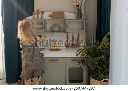A young child smiles while playing with toy kitchen toys in a well-decorated, light-filled room. Eco-friendly and safe handmade wooden products for children development and learning. 