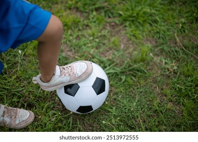 A young child is standing on a soccer ball in a grassy field. Concept of innocence and playfulness, as the child is engaged in a simple, enjoyable activity - Powered by Shutterstock