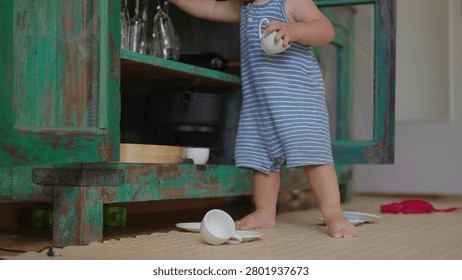Young child standing while playing with cups taken from cabinet capturing toddler independence movement and natural curiosity in home kitchen environment