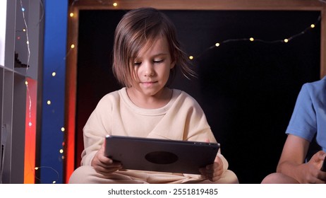 Young child using tablet computer at home with fairy lights in background