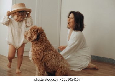 A young child wearing a straw hat plays with a fluffy dog in a bright room, while a woman sits nearby laughing. The cheerful atmosphere highlights their joyful interaction - Powered by Shutterstock