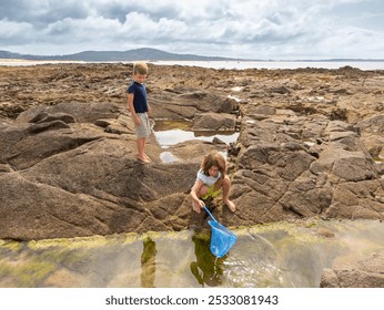 Young children boy and girl playing outdoors at a seaside rock pool with fishing net in  Galicia, Spain - Powered by Shutterstock