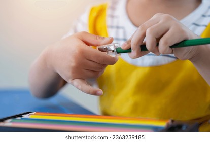 Young children hands using pencil sharpener for sharpening colored pencils. Education concept, selective focus.