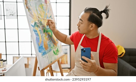 Young chinese artist immersed in drawing via smartphone, embracing tech creativity at art studio - Powered by Shutterstock