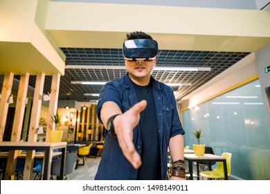 Young Chinese businessman working in office with virtual reality glasses on head. Man using VR headset for handshaking in augmented reality - Powered by Shutterstock