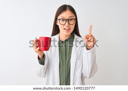 Young chinese dooctor woman wearing glasses drinking coffee over isolated white background surprised with an idea or question pointing finger with happy face, number one