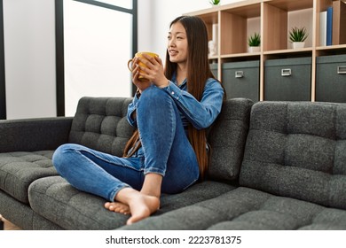 Young Chinese Girl Drinking Coffee Sitting On The Sofa At Home.