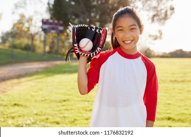 Young Chinese girl holding baseball in mitt looks to camera