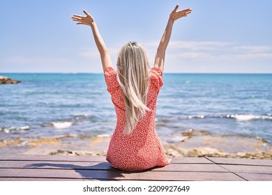 Young Chinese Girl On Back View Sitting On The Bench With Hands Raised Up At The Beach.