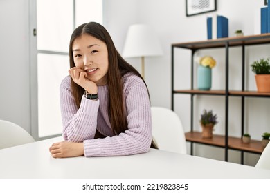 Young Chinese Girl Smiling Happy Sitting On The Table At Home.