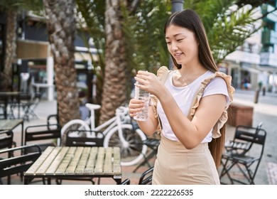 Young Chinese Girl Smiling Happy Drinking Water At The City.