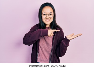 Young chinese girl wearing casual clothes and glasses amazed and smiling to the camera while presenting with hand and pointing with finger.  - Shutterstock ID 2079078613