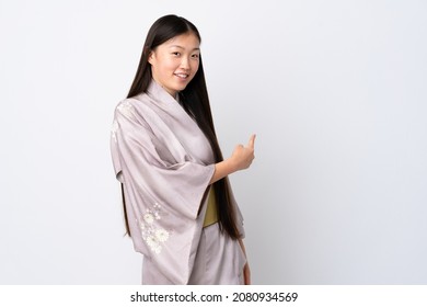 Young Chinese Girl Wearing Kimono Over Isolated Background Pointing Back