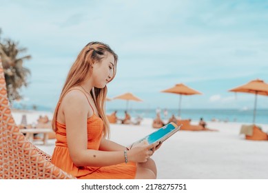 A Young Chinese Lady In An Orange Dress Reading A Magazine By The Beach. A Mellow And Relaxing Moment At The Resort.